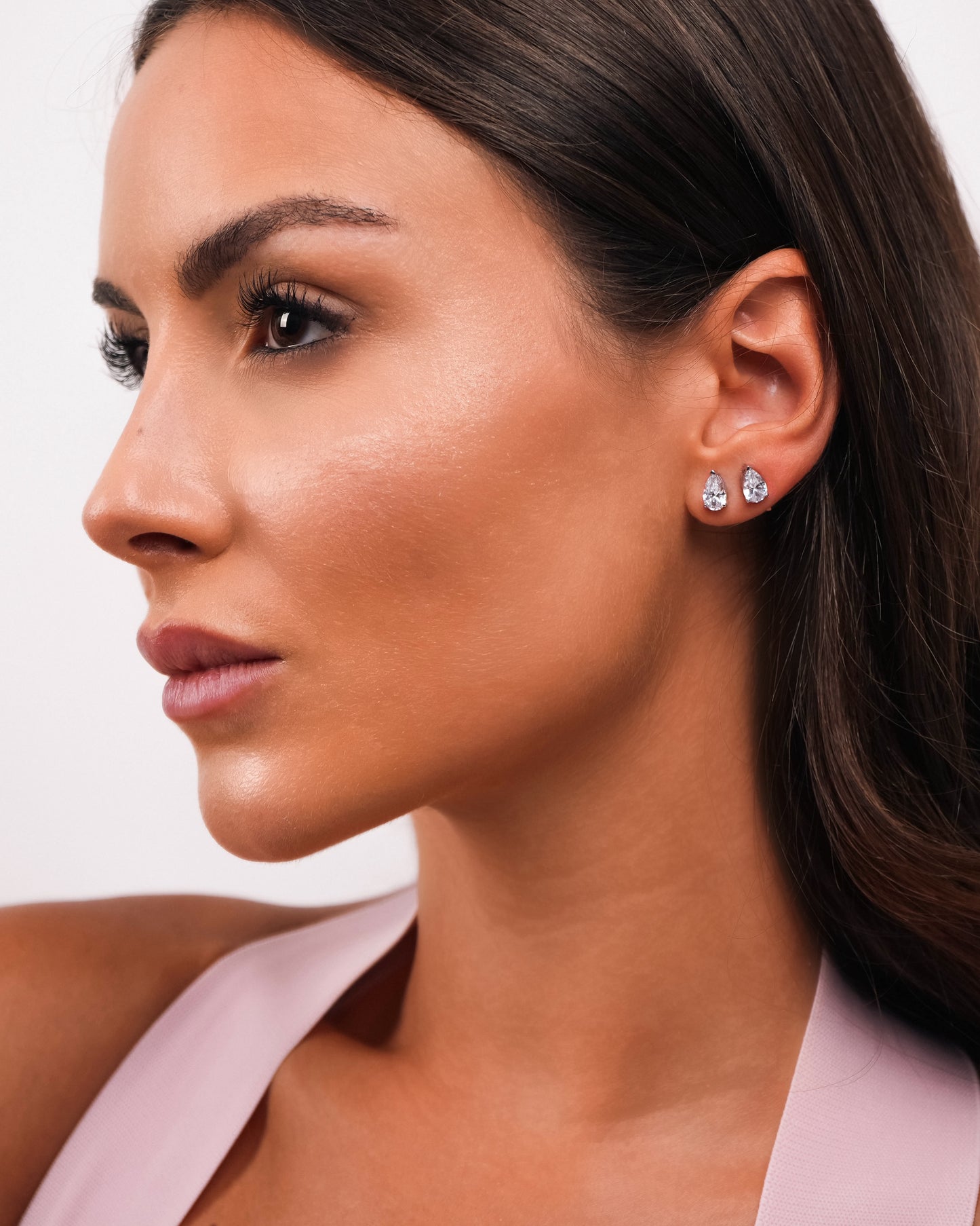 Close-up of a woman wearing diamond stud earrings by lucky13 jewelry with a plain background
