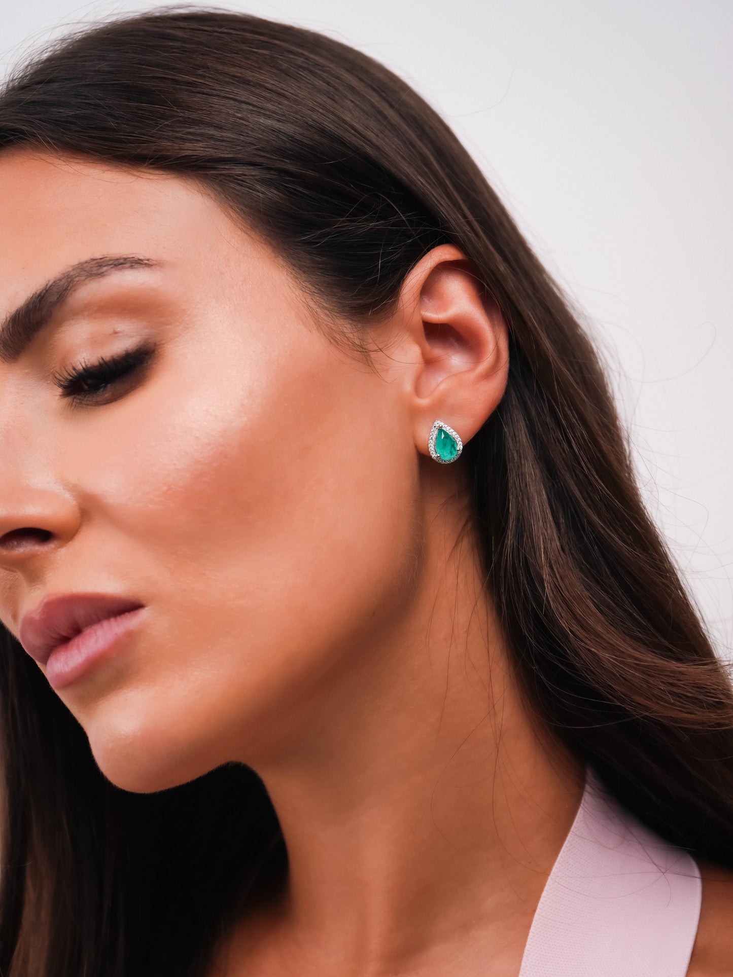 Close-up of a woman wearing a green gemstone earring against a neutral background