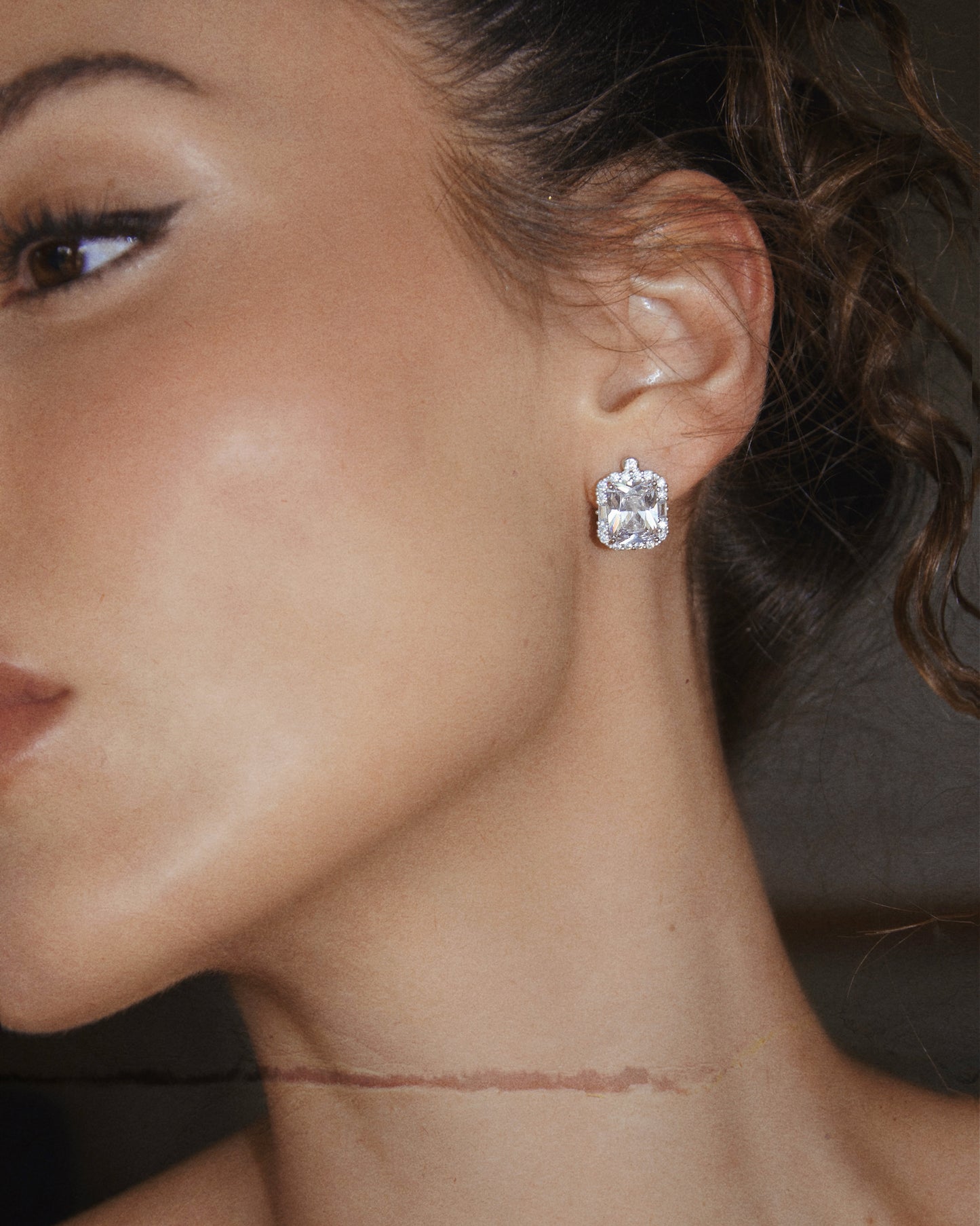 Close-up of a woman's profile showcasing her clear skin and elegant LUCKY13 VINTAGE DIAMOND STUDS earring. Her hair is styled in soft curls, and she wears subtle makeup with winged eyeliner. The focus is primarily on the hand-finished earring and her smooth complexion.